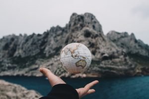 hand throwing small globe in front of mountain