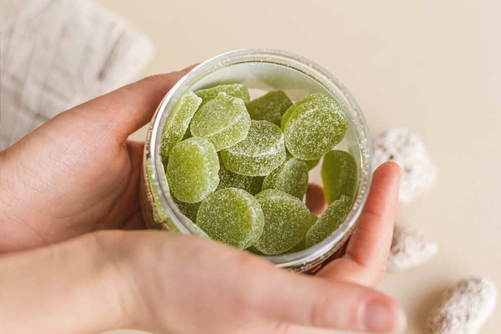 hands holding glass jar of green gummy sweets
