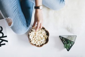 person in jeans eating popcorn from bowl